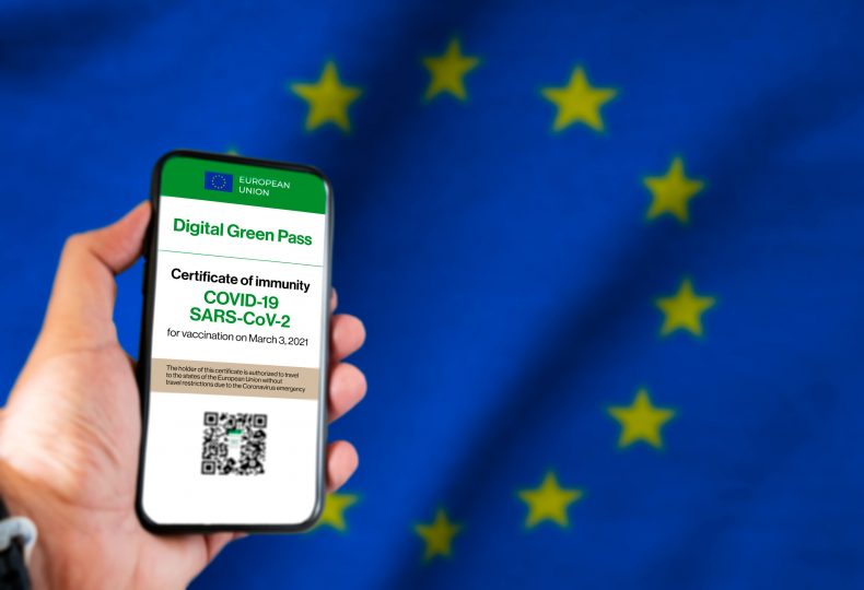 The digital green pass of the european union with the QR code on the screen of a mobile held by a hand with a blurred EU flag in the background